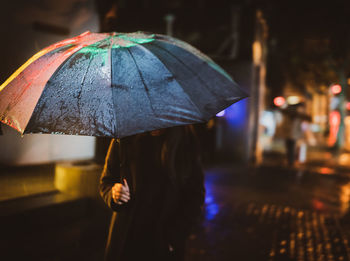 Person holding umbrella standing on wet street during rainy season