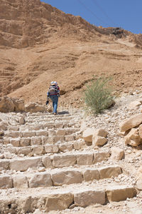 Rear view of woman walking on mountain carrying baby on the back. 