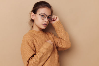 Portrait of girl wearing eyeglasses against beige background
