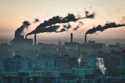 Smoke emitting from factory against sky during sunset