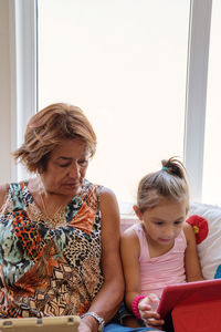 Grandmother sitting with her granddaughter helping her to do e-learning