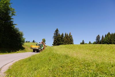 People riding motorcycle on field against clear blue sky