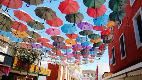 Low angle view of multi colored umbrellas hanging amidst buildings