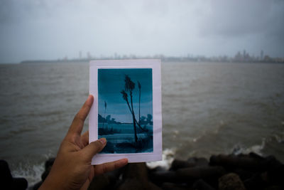 Person holding umbrella by sea against sky