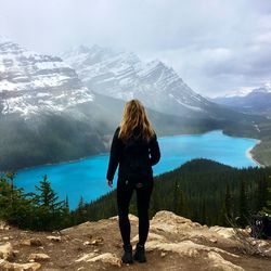 Rear view of woman standing on cliff against mountain against sky