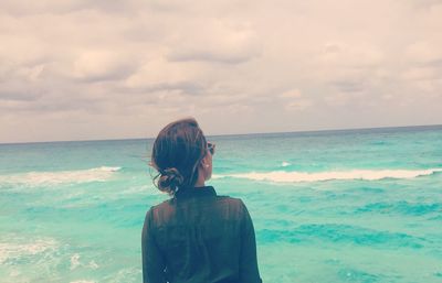 Rear view of woman standing on shore against sky