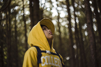 Low angle portrait of man standing against trees in forest