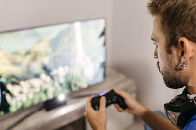 Young man holding controller while playing video game at home