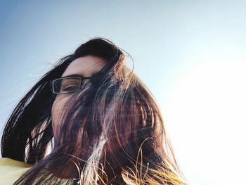 Low angle portrait of woman with long hair against bright sky