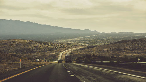 Country road leading towards mountains against sky