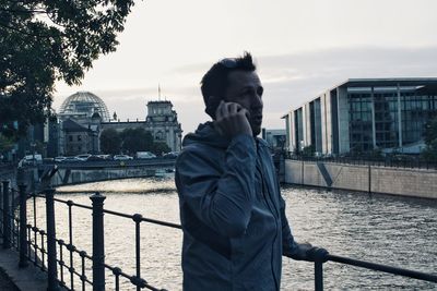 Man standing on railing with river in city