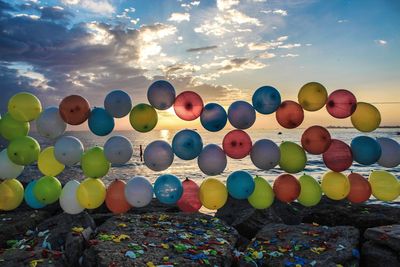 Multi colored balloons at beach against sky during sunset