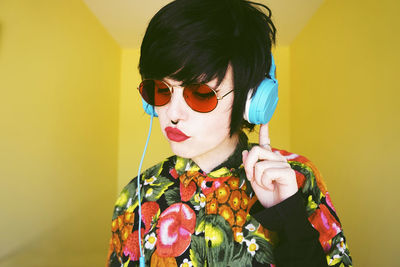 Hipster woman listening music against yellow wall