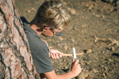 High angle view of boy cutting stick in forest