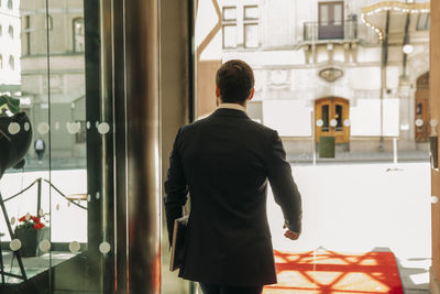 Rear view of young businessman with laptop leaving hotel