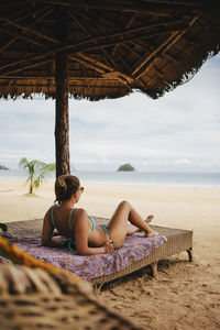 Woman in bikini relaxing on bed at beach