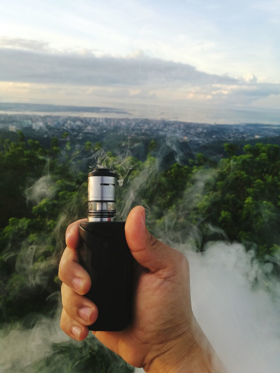 HUMAN HAND HOLDING BOTTLE AGAINST SKY