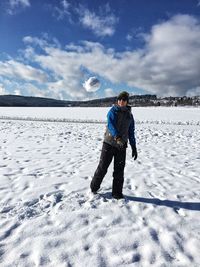 Teenage boy throwing snowball while standing on field against sky