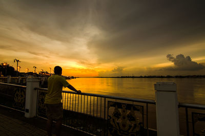 Rear view of man looking at sea against sky during sunset