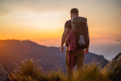 Rear view of people standing on land against sky during sunset