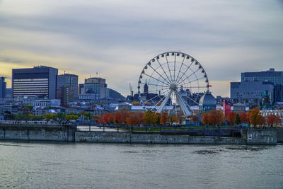 Ferris wheel by river in city against sky