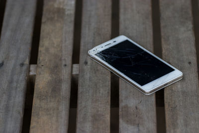 High angle view of cracked mobile phone on wooden table