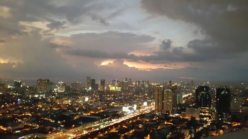 Aerial view of illuminated cityscape against cloudy sky