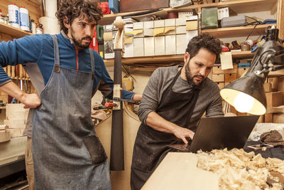 Two craftsmen violinmakers checking data and measures for a new violin with computer