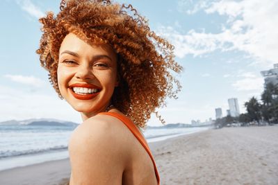 Portrait of young woman at beach against sky