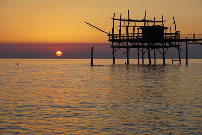 Silhouette built structure over sea against sky during sunset