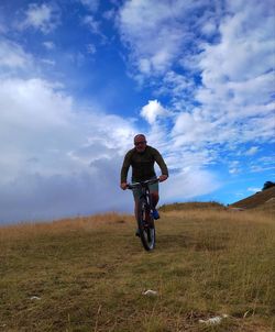 Rear view of man riding bicycle on field against sky
