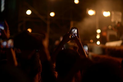 Midsection of woman photographing illuminated smart phone at music concert