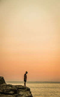 Side view of mature man standing on rock by sea against sky during sunset