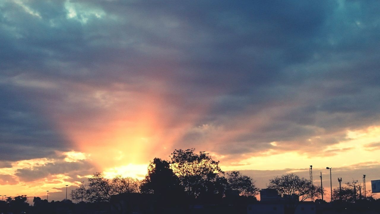 sunset, sky, silhouette, cloud - sky, beauty in nature, orange color, tree, scenics, dramatic sky, cloudy, tranquility, nature, low angle view, tranquil scene, cloud, idyllic, moody sky, building exterior, weather, built structure