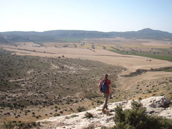 Rear view of man hiking in desert against clear sky