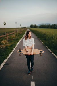 Young woman holding skateboard standing on road