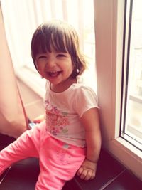 High angle portrait of baby girl laughing while sitting by window at home
