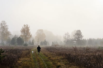 Woman with dog walking on land during foggy weather