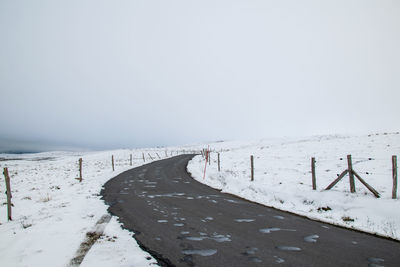 Snow covered road amidst field against sky