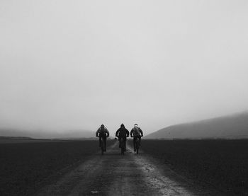 Rear view of men riding bicycles on road in foggy weather