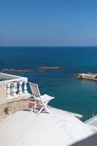 Chairs by swimming pool against sea against clear sky