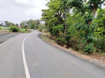 Empty road amidst trees against sky