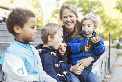 Happy teacher sitting with children outside kindergarten