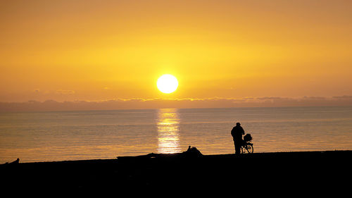 Silhouette man by sea against orange sky during sunset