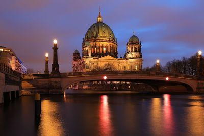 Illuminated cathedral over river against sky at night