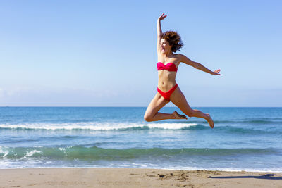 Full length of woman jumping at beach against clear sky
