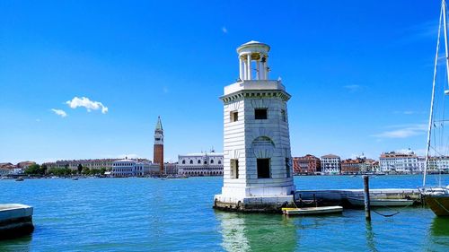 Lighthouse by sea against buildings in city