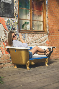 Young woman sitting on bathtub seat against brick wall