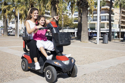 Smiling mother and daughter sitting on motorized wheelchair