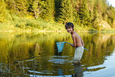 Boy standing in lake against trees